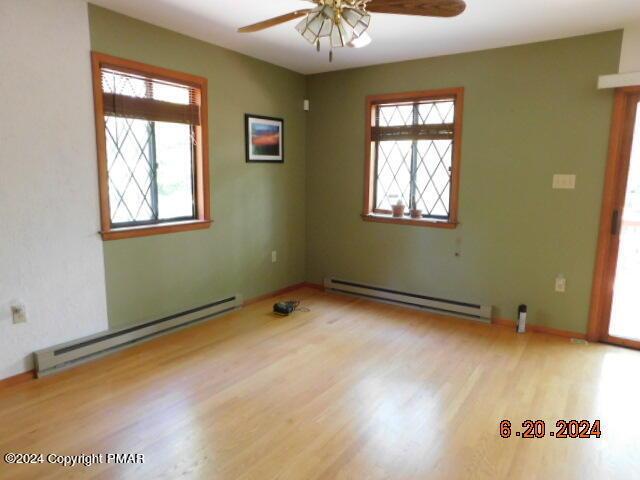 spare room featuring a baseboard heating unit, wood finished floors, baseboards, and ceiling fan