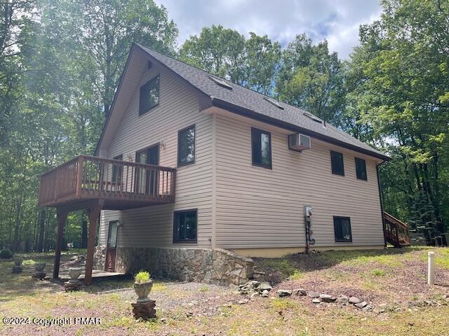 view of home's exterior featuring a wall mounted air conditioner, a wooden deck, and roof with shingles