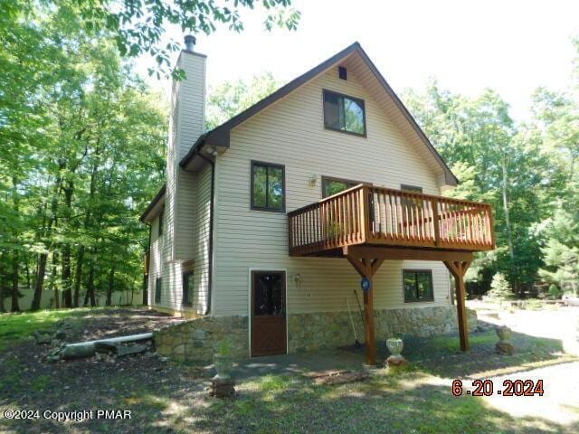 back of property featuring stone siding, a deck, and a chimney