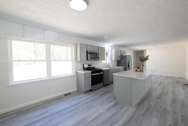 9133 Belvedere Rd # 5020, Tobyhanna, PA 18466 - kitchen featuring stainless steel appliances, gray cabinets, a textured ceiling, a center island, and light wood-type flooring
