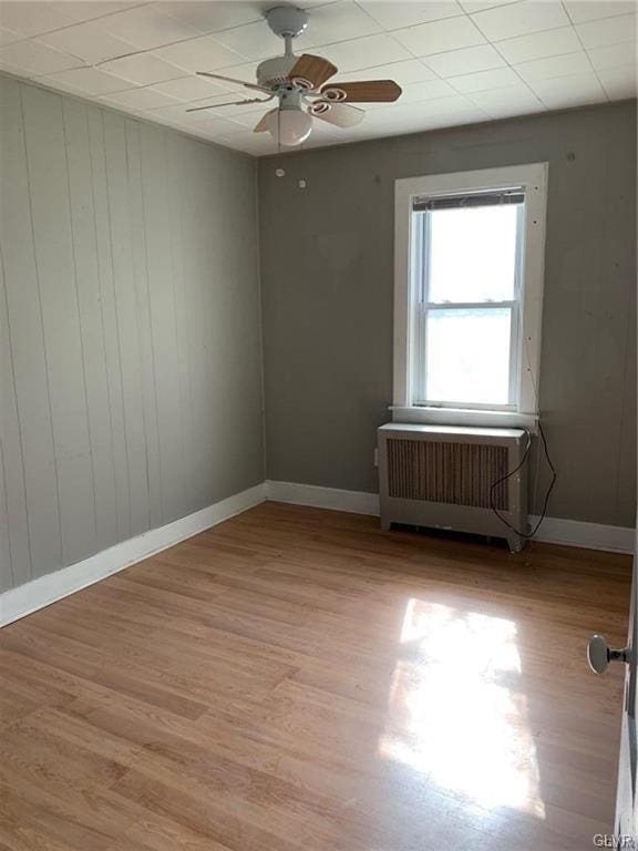 unfurnished room featuring baseboards, ceiling fan, radiator heating unit, and light wood finished floors