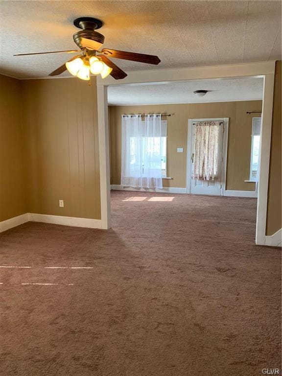 carpeted empty room featuring a textured ceiling, baseboards, wood walls, and ceiling fan