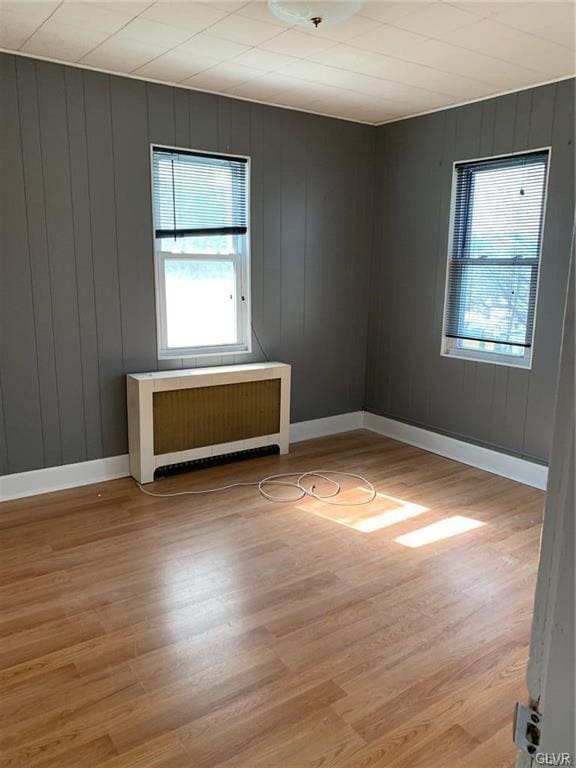 empty room featuring light wood-style flooring, radiator, and baseboards