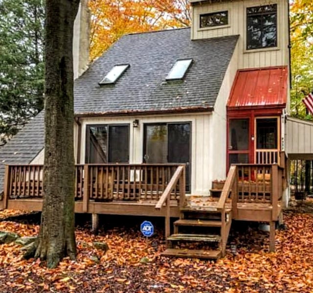 rear view of house with board and batten siding, roof with shingles, a deck, and a chimney
