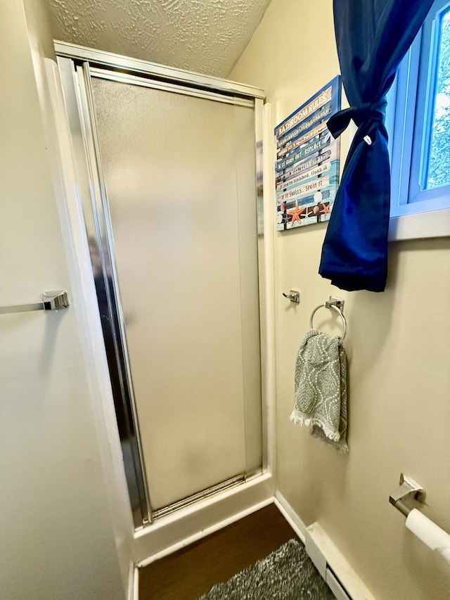 full bath featuring a shower stall, baseboards, a baseboard heating unit, and a textured ceiling