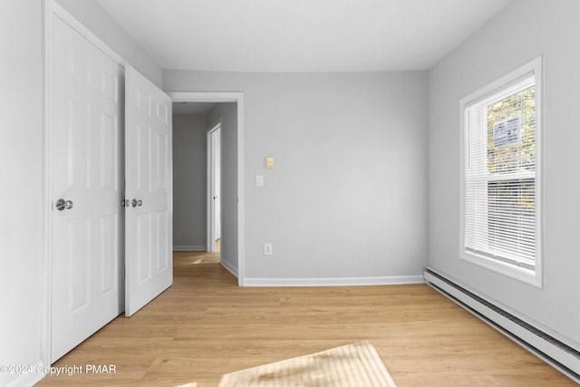 unfurnished bedroom with light wood-style flooring, a baseboard heating unit, and baseboards