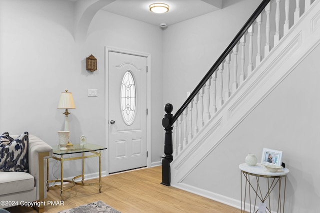 foyer with stairs, light wood finished floors, arched walkways, and baseboards