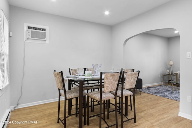 dining space with light wood finished floors, arched walkways, baseboards, a baseboard radiator, and a wall mounted AC