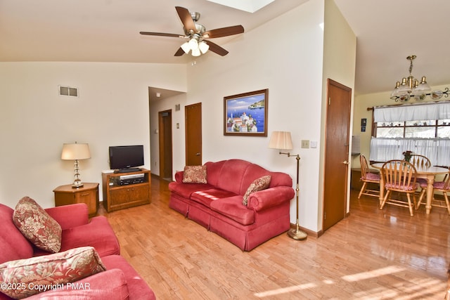 living area with ceiling fan with notable chandelier, high vaulted ceiling, light wood finished floors, and visible vents