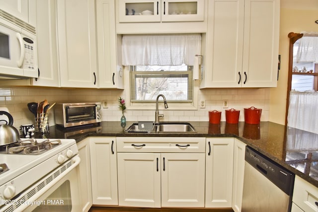 kitchen with a toaster, white appliances, a sink, white cabinetry, and dark stone counters