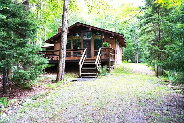 view of front of home with a forest view, stairway, a chimney, and gravel driveway