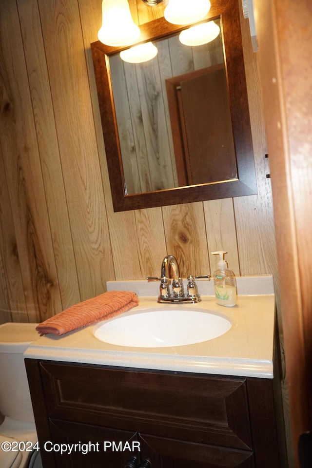 bathroom featuring toilet, vanity, and wooden walls