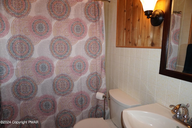 bathroom with toilet, curtained shower, a sink, and tile walls