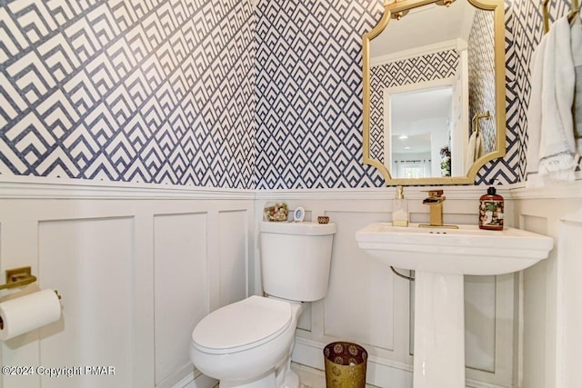 half bath with wallpapered walls, a decorative wall, toilet, and crown molding