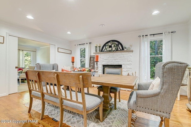 dining space featuring a stone fireplace, light wood finished floors, recessed lighting, and crown molding