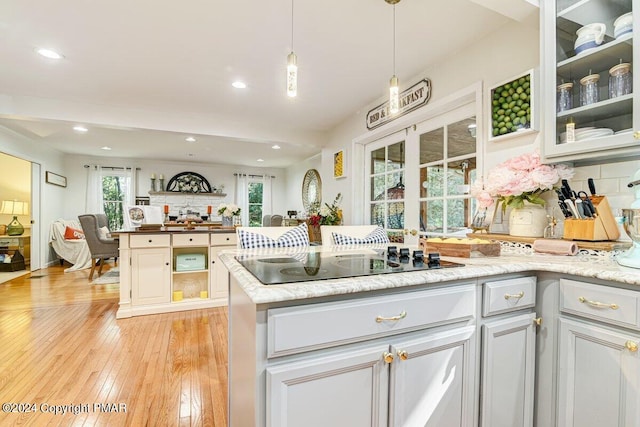 kitchen with open floor plan, light wood-style flooring, black electric cooktop, and tasteful backsplash