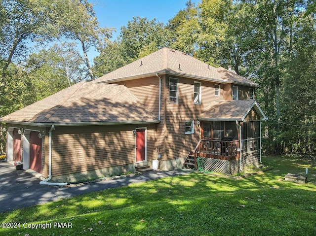 rear view of house with a garage, a lawn, a sunroom, aphalt driveway, and roof with shingles