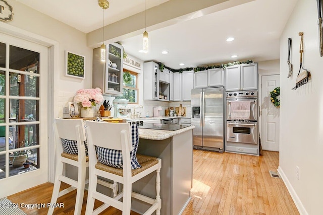 kitchen with tasteful backsplash, appliances with stainless steel finishes, a breakfast bar area, a peninsula, and light wood-type flooring