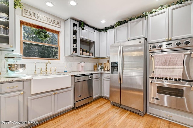 kitchen with decorative backsplash, glass insert cabinets, stainless steel appliances, light wood-type flooring, and a sink