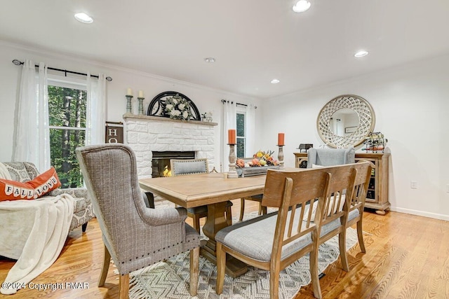 dining area with crown molding, recessed lighting, a fireplace, and light wood-style floors