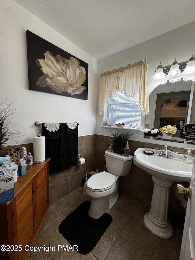 half bath featuring wainscoting, tile patterned flooring, toilet, and tile walls