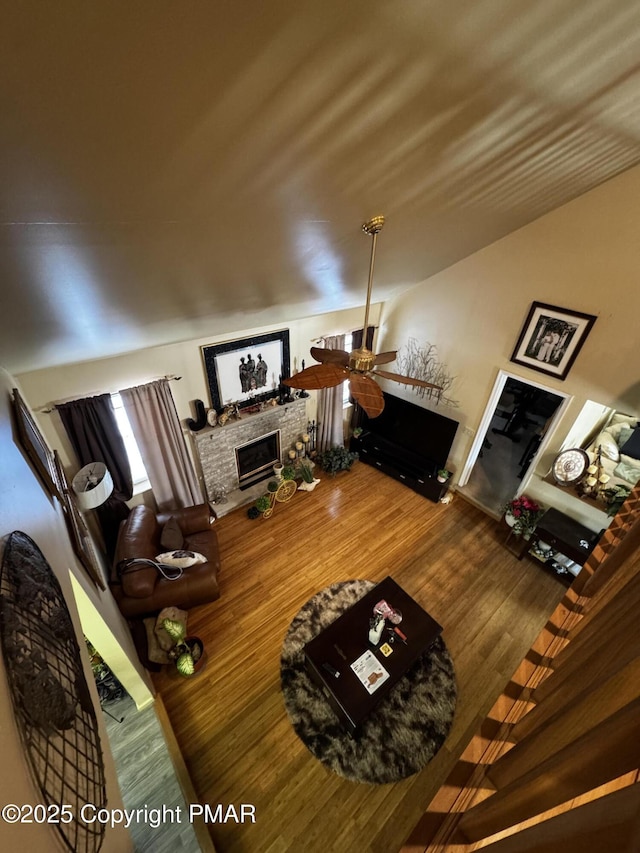 living area featuring a ceiling fan, wood finished floors, and a stone fireplace