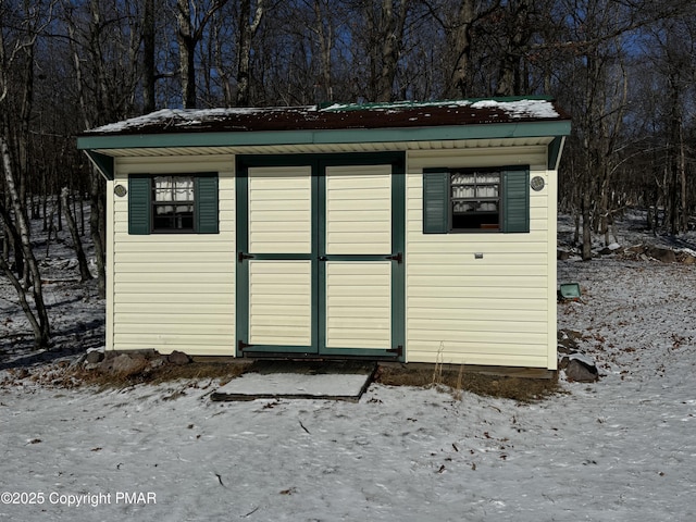 snow covered structure featuring an outbuilding and a storage unit