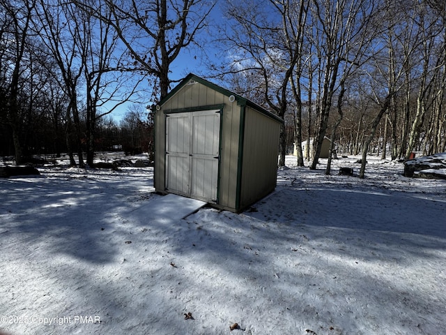 snow covered structure featuring a storage unit and an outbuilding