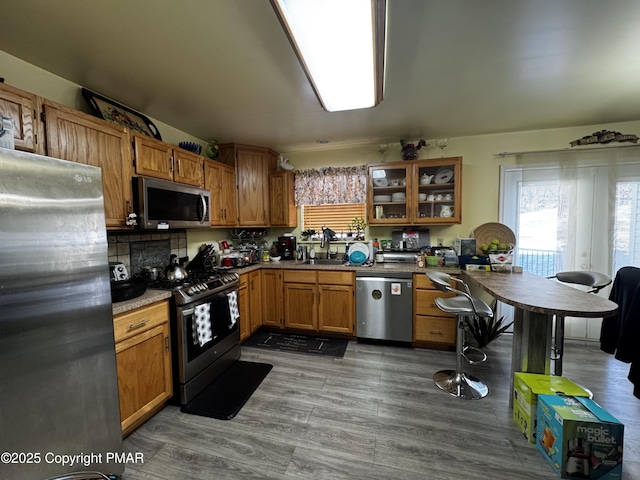 kitchen featuring glass insert cabinets, appliances with stainless steel finishes, brown cabinetry, and dark wood finished floors