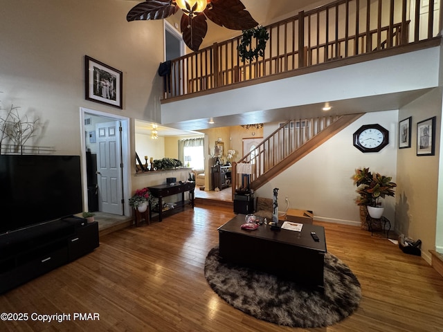 living area with a high ceiling, ceiling fan, wood finished floors, baseboards, and stairs