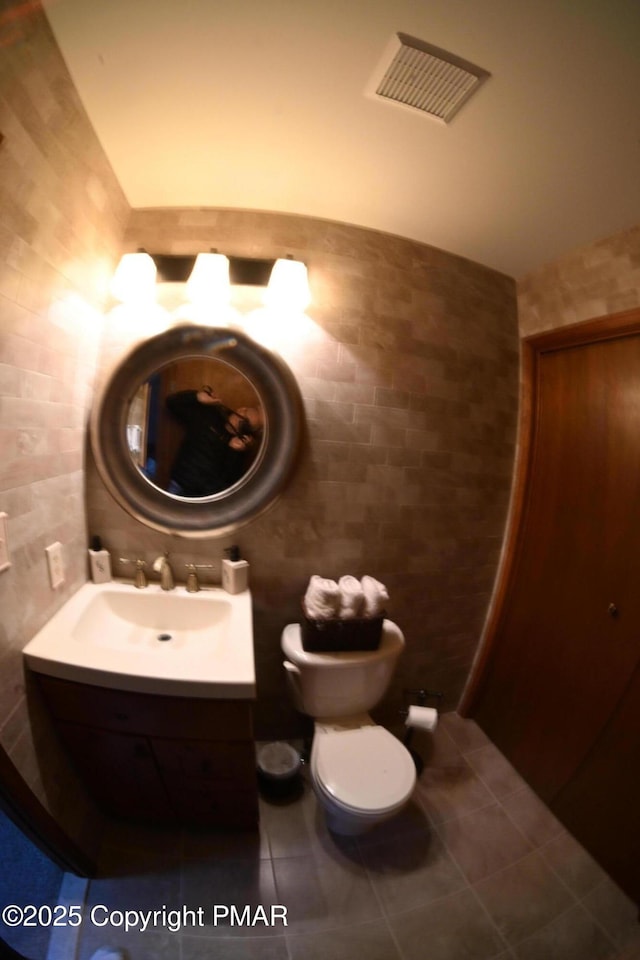 half bathroom with visible vents, tile walls, vanity, and tile patterned floors