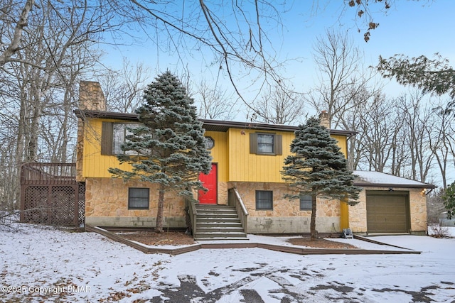 split foyer home with stone siding, a chimney, and an attached garage