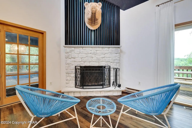 sitting room with a wealth of natural light, baseboard heating, a fireplace with raised hearth, and wood finished floors