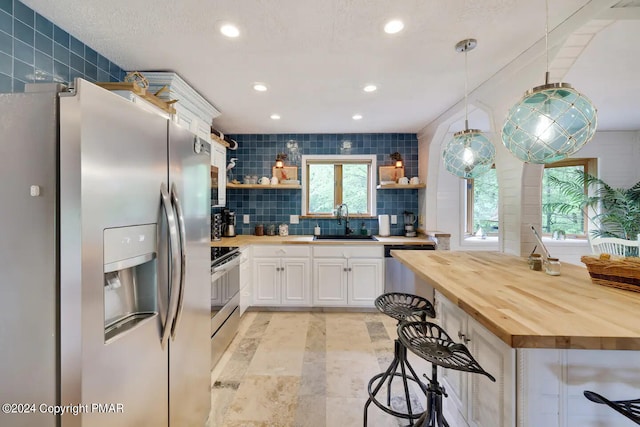 kitchen with a sink, wood counters, appliances with stainless steel finishes, decorative backsplash, and open shelves