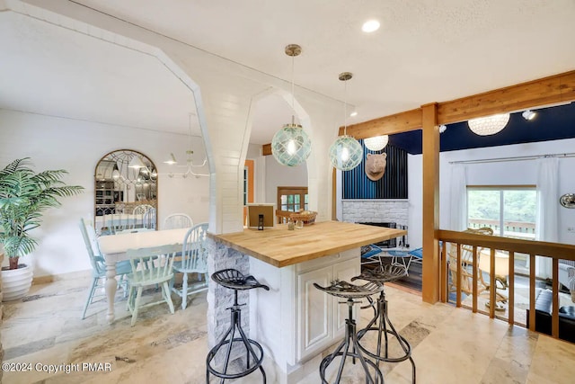 kitchen with butcher block countertops, a breakfast bar, a kitchen island, hanging light fixtures, and beam ceiling