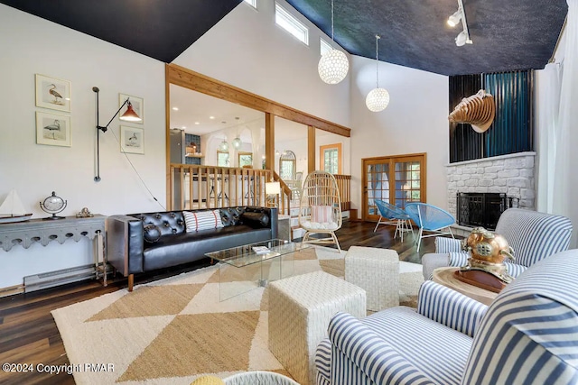 living area with a healthy amount of sunlight, a stone fireplace, a high ceiling, and wood finished floors