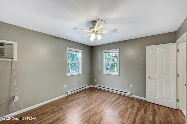 unfurnished bedroom with hardwood / wood-style flooring, a baseboard radiator, an AC wall unit, and ceiling fan