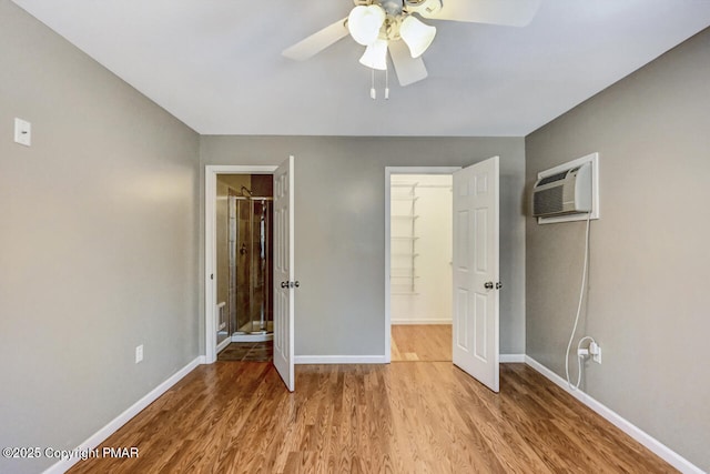 unfurnished bedroom with connected bathroom, a walk in closet, a wall mounted air conditioner, ceiling fan, and light hardwood / wood-style floors