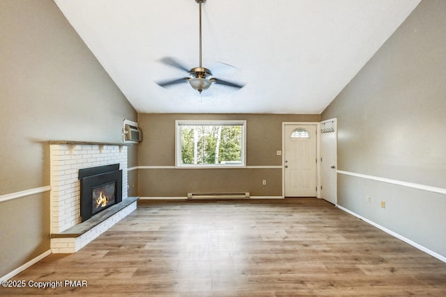 unfurnished living room featuring vaulted ceiling, a baseboard radiator, a wall mounted AC, a brick fireplace, and light wood-type flooring