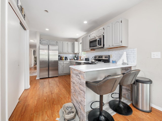 1533 Black Birch Way, Tobyhanna, PA 18466 - kitchen featuring stainless steel appliances, a peninsula, light wood-type flooring, a kitchen bar, and backsplash