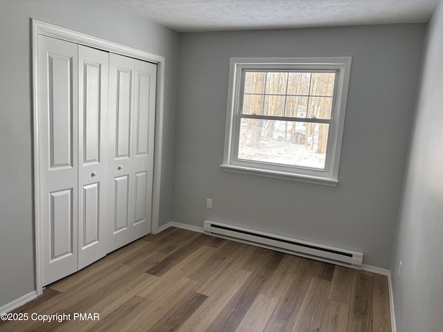 unfurnished bedroom featuring a closet, baseboard heating, wood finished floors, and a textured ceiling