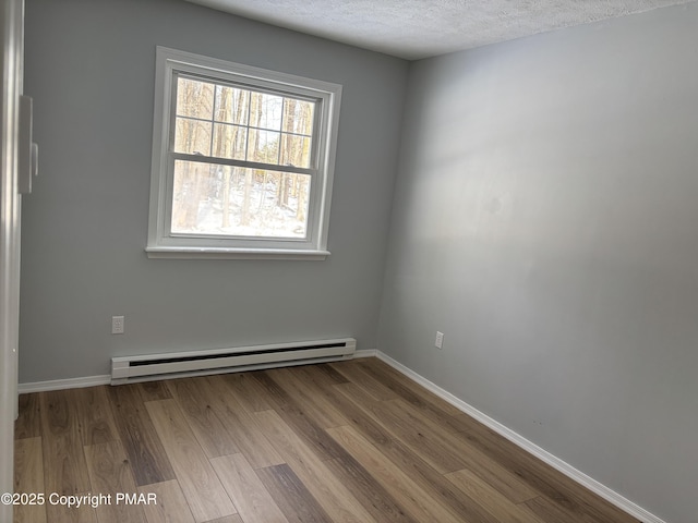 unfurnished room with baseboards, a textured ceiling, a baseboard heating unit, and wood finished floors