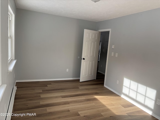 spare room with a baseboard heating unit, a textured ceiling, wood finished floors, and baseboards