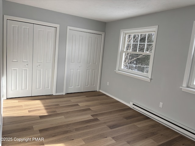 unfurnished bedroom featuring wood finished floors, a baseboard radiator, two closets, and baseboards