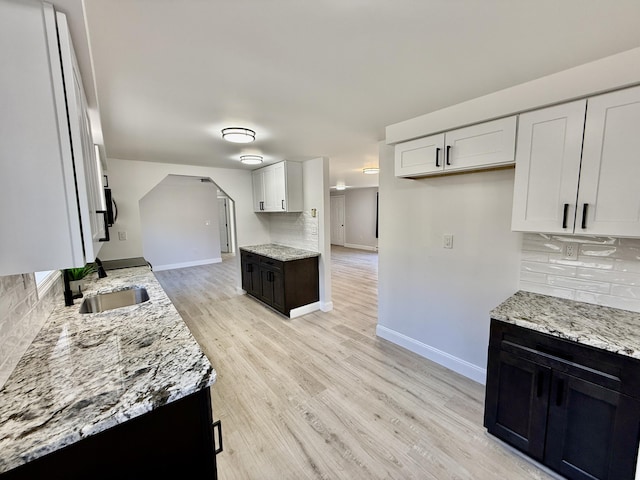 kitchen with baseboards, light stone counters, decorative backsplash, light wood-style flooring, and a sink