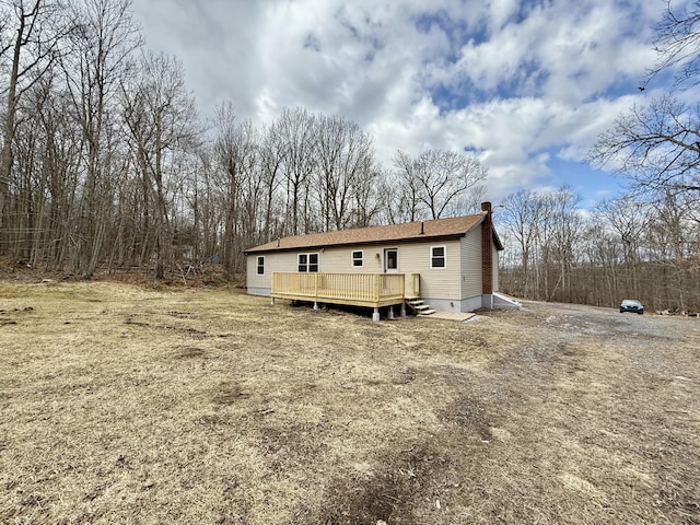 back of house featuring a chimney, a deck, and dirt driveway