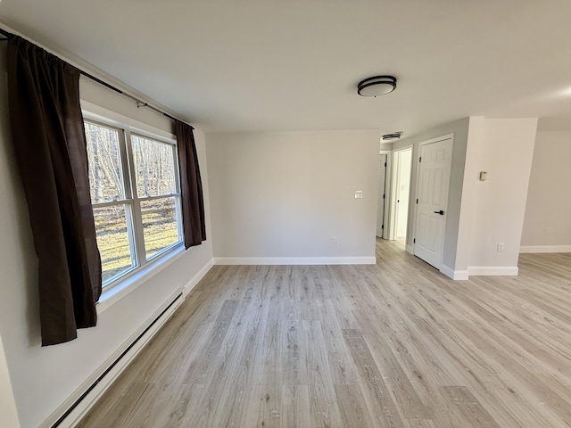 empty room featuring baseboards, light wood finished floors, and a baseboard radiator