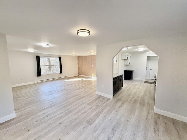 unfurnished living room featuring arched walkways, light wood-style flooring, baseboards, and a baseboard radiator