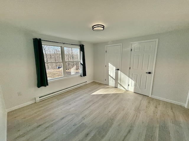 unfurnished bedroom featuring baseboards, baseboard heating, wood finished floors, and a textured wall