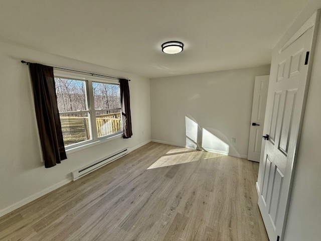 unfurnished room featuring a baseboard heating unit, baseboards, and light wood-type flooring